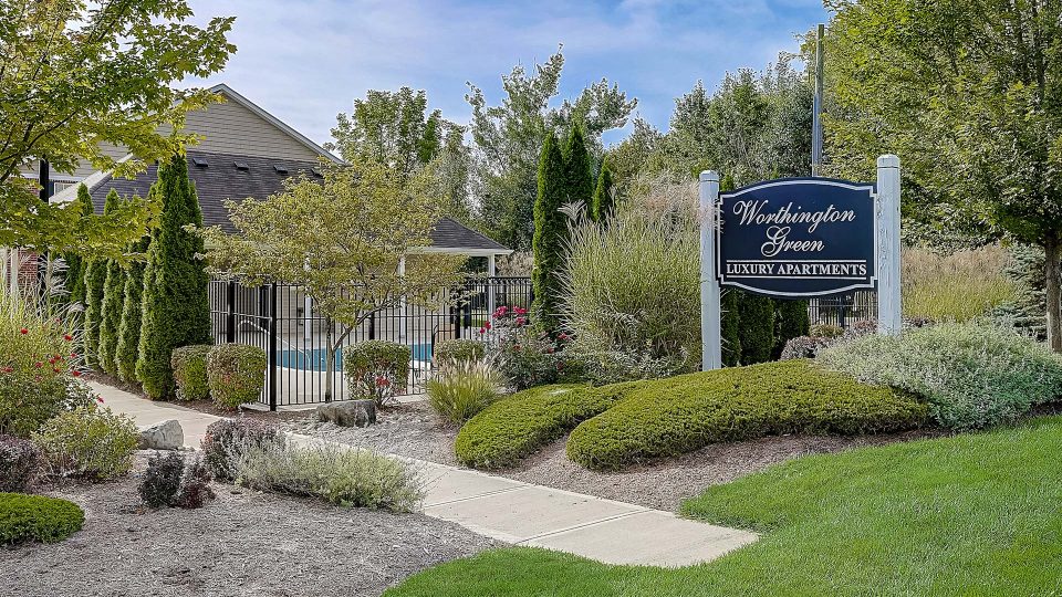 the entrance to a residential community with landscaping and trees at The Worthington Green